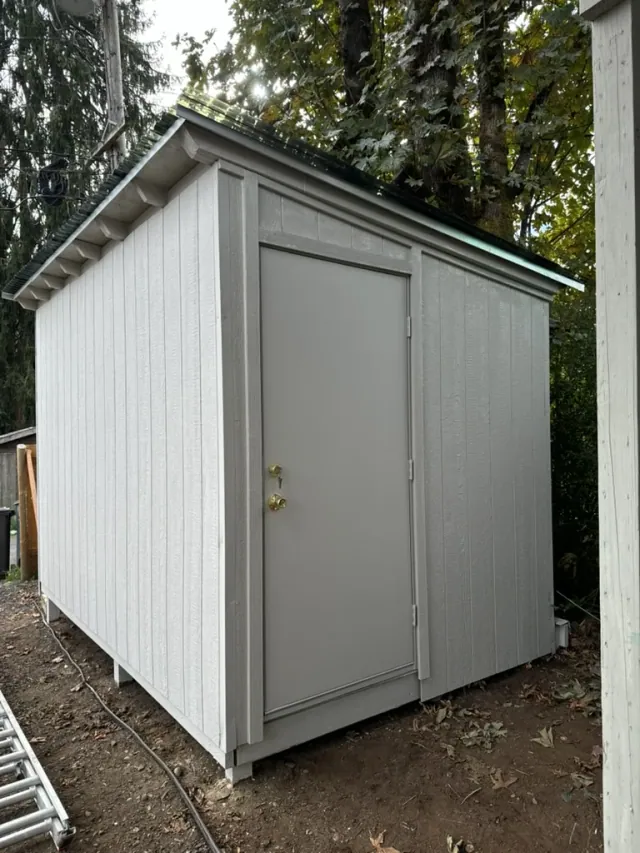 Completed custom shed with painted vertical siding, door trim, and sloped roof