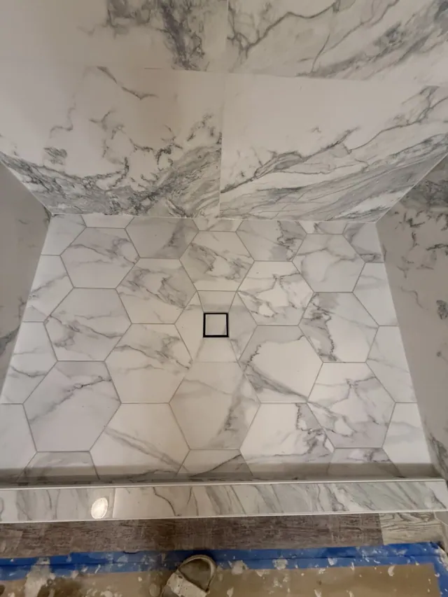 Hexagonal marble-look shower floor tiles around a square tile-in drain