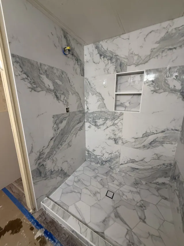 Marble-look shower wall tile with a recessed shelf niche and hexagonal floor