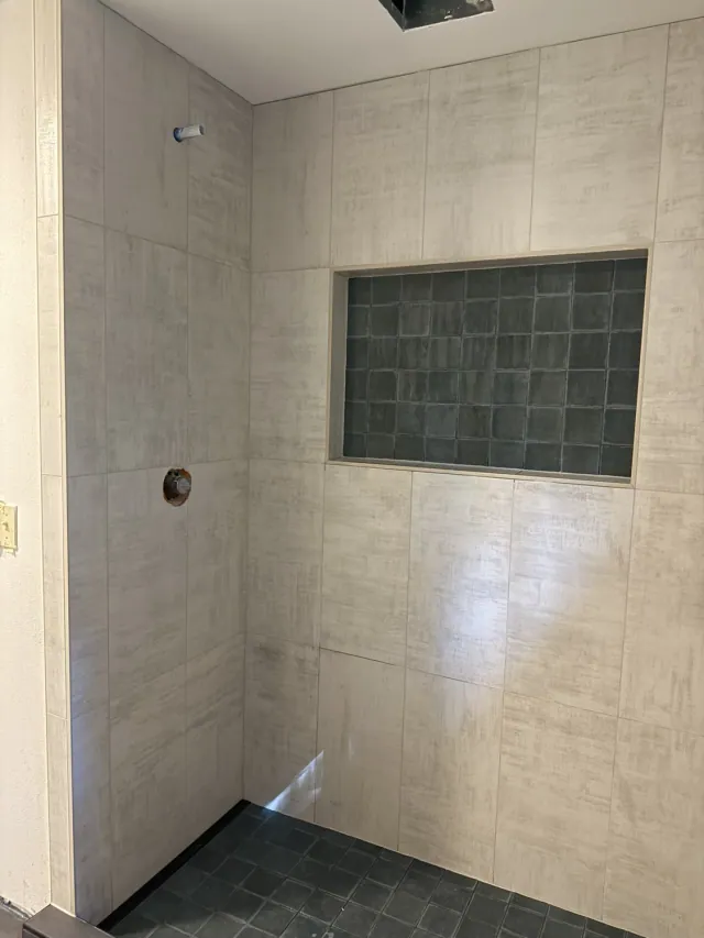 Beige shower wall tiles with a dark tiled recessed niche and matching square shower floor tiles by Remodel Tsaruk LLC