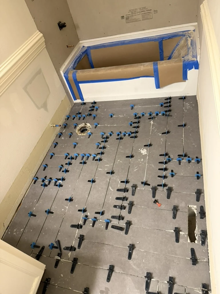 Bathroom floor tile installation in progress beside a protected tub